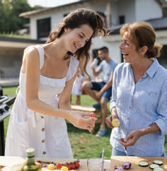 2 women stand around a table filled with various dishes, engaged in conversation and enjoying the meal together.